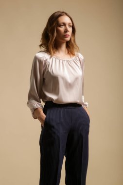 Çizgili sigara pantolonu ve bej bluz giyen kadın model, stüdyo fotoğrafı..