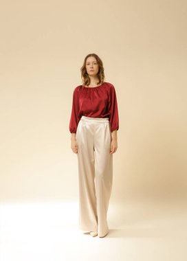 Stüdyo fotoğrafları, sade ipek saten elbiseler, bordo bluz ve bej geniş paça pantolon giyen genç kadın modeller..