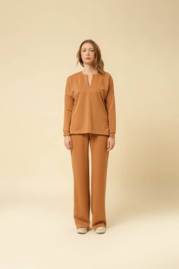 Loungewear pamuk giyen kadın model yumuşak ve rahat kıyafet, bej bluz ve pantolon. Klasik ve basit moda. Stüdyo çekimi.