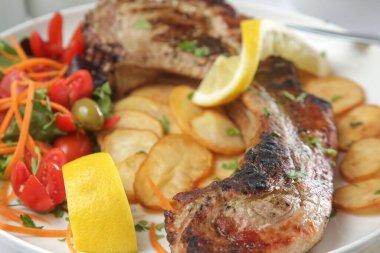 Patates ve yeşil salatayla servis edilen kaburga kemikli domuz pirzolası