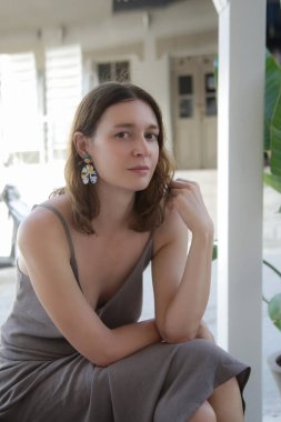 Camisole keten elbiseli güzel bir kadın balkonda oturuyor, tembel bir yaz öğleden sonra.