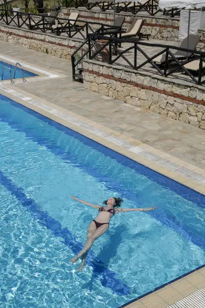 Genç bir kadın yüzme havuzunda yüzüyor.