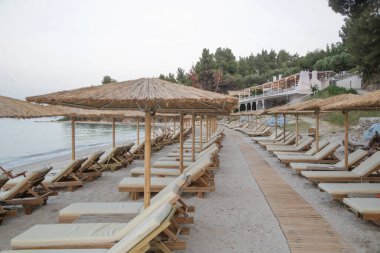 Boş plaj, saman şemsiyeler ve tahta güneşlikler.