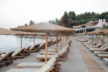 Boş plaj, saman şemsiyeler ve tahta güneşlikler.