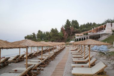 Boş plaj, saman şemsiyeler ve tahta güneşlikler.