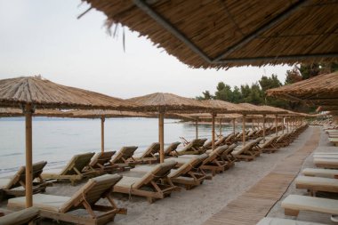 Boş plaj, saman şemsiyeler ve tahta güneşlikler.