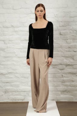 Stüdyo fotoğrafı, basit güzel kıyafetler, siyah gömlek ve bej geniş paça pantolon giyen genç bir kadın manken. 