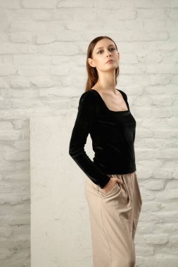 Stüdyo fotoğrafı, basit güzel kıyafetler, siyah gömlek ve bej geniş paça pantolon giyen genç bir kadın manken. 