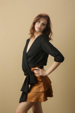 Siyah bluz ve bej mini etek giyen kadın model. Şık ve şık bir kıyafet. Moda Stüdyosu çekimi.