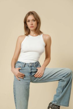 Klasik kıyafetli bir kadının stüdyo fotoğrafları. Mavi kot pantolon ve beyaz atlet.