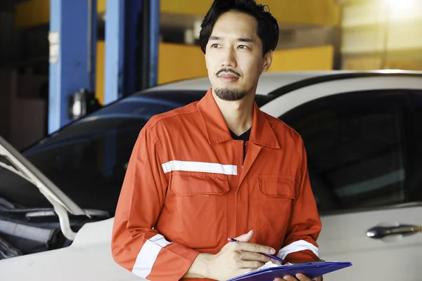 Standing Reviewing Report. Car Repairman Auto Mechanic Working In Garage With Automobile. Repair service. Selective Focus.