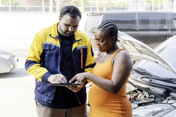 Mechanic holding a clipboard and showing the car checking list and repaired item to woman customer in the garage, Auto car repair service center, Professional service, Selective Focus