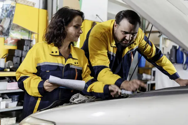 Vehicle service maintenance man and woman checking with notepad in hand  under car in garage. A car maintenance worker is checking a list of the car interior for workshop customer. Teamwork. Car repair maintenance. Selective Focus