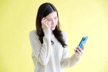 Stresli Asyalı kadın cep telefonuyla boğuşuyor, Asyalı kadın elinde akıllı telefon tutarken sarı izole edilmiş arka planda duruyor, insanlar teknolojiyle boğuşuyor.