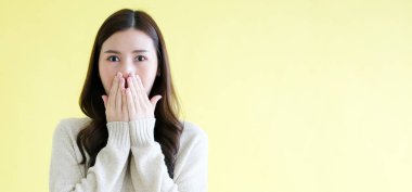 Genç Asyalı kadın şaşırdı ve kameraya baktı. Bu sırada da izole edilmiş sarı arka planda fotokopi alanı ile duruyordu.