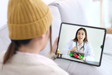 Asyalı kadın hasta dijital tablet, teletıp, eczacı, sağlık hizmetleri hakkında danışmanlık yapıyor.
