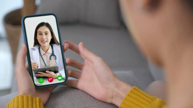 Asyalı kadın hasta, cep telefonu, teletıp, eczacı gibi sağlık hizmetleri hakkında danışmanlık yapıyor.