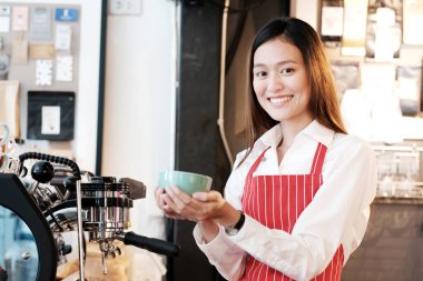 Kafe arka planında gülümseyen yüzlü genç Asyalı kadın barista, küçük işletme sahibi, yiyecek ve içecek endüstrisi konsepti