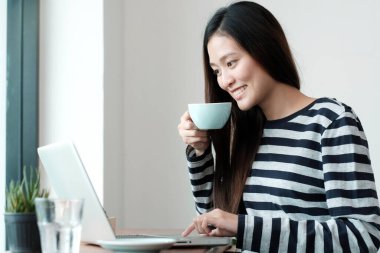 Genç Asyalı kadın dizüstü bilgisayar kullanıyor ve kafenin arka planında kahve içiyor, insanlar ve teknoloji, yaşam tarzları