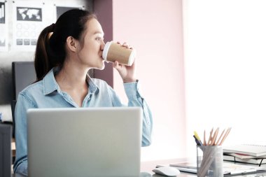 Masa başında çalışırken kahve içen Asyalı genç ofis kadını, ofis yaşam tarzı konsepti.