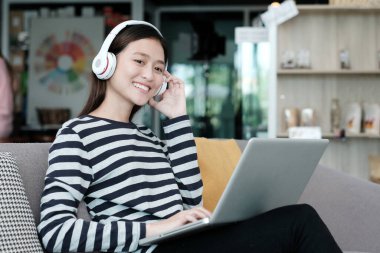 Kablosuz kulaklık takan genç ofis kadını dizüstü bilgisayarla, günlük yaşam tarzlarıyla, insanlarla ve teknolojiyle çalışırken dinleniyor.