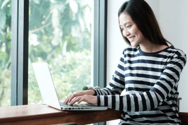 Genç Asyalı kadın kafede dizüstü bilgisayar kullanıyor. Günlük yaşam tarzları, insanlar ve teknoloji, yaşam tarzları.