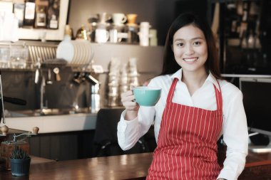 Kafe arka planında gülümseyen yüzlü genç Asyalı kadın barista, küçük işletme sahibi, yiyecek ve içecek endüstrisi konsepti