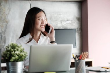 Ofis masasında çalışırken akıllı telefonlardan konuşan genç iş kadını, iş adamları ve iletişim konsepti, ofis hayatı.