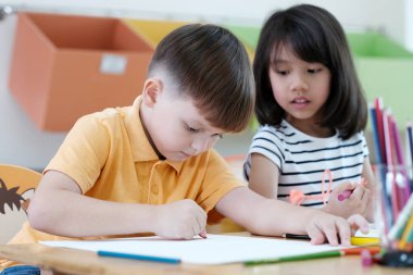 Anaokulunda, anaokulunda ve çocuk eğitim konseptinde renkli kalemler çizen kız ve erkek çocuk.