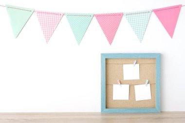 Mavi antika ahşap çerçevenin üzerinde asılı renkli parti bayrakları ve beyaz arka planda fotokopi alanı, doğum günü, yıldönümü, kutlama etkinliği, festival arka planı olan boş kağıt kağıtlar.