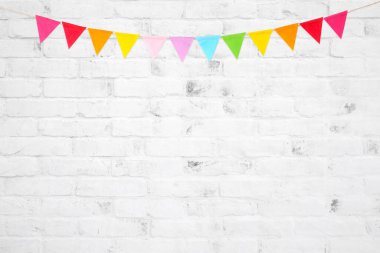 Beyaz tuğla duvarda asılı renkli parti bayrakları, doğum günü, yıldönümü, kutlama etkinliği, festival tebrik kartı geçmişi