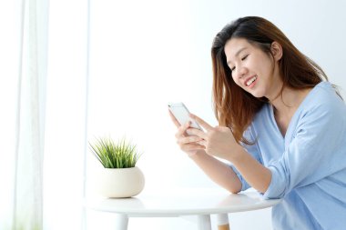 Genç Asyalı kadın akıllı telefon kullanıyor. Beyaz arka planda rahatlama duygusu, telefondaki insanlar, yaşam tarzı.