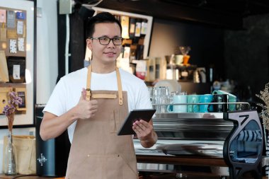 Genç Asyalı adam, barista, kafenin arka planında tablet kullanıyor, yiyecek ve içecek konsepti.