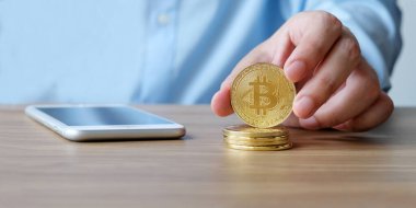 El ele tutuşan bitcoin ve akıllı telefon ofis masasında arka planda, taklit, engelleme zinciri ve kripto para kavramı arka plan