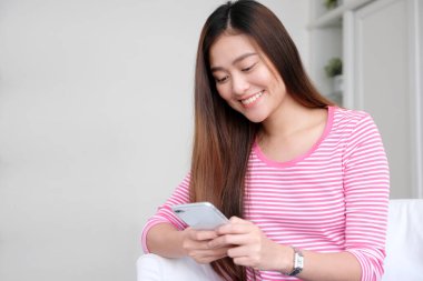 Genç asyalı kadın gülümseyen ile akıllı telefon kullanarak, mutlu ve beyaz oda arka planda duygu dinlenmek, telefonda insanlar, yaşam tarzı