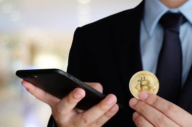 İş adamı elinde bitcoin tutuyor ve arka planda akıllı telefon kullanıyor, taklit et, engelleme zinciri ve kripto para birimi konsepti arka planı