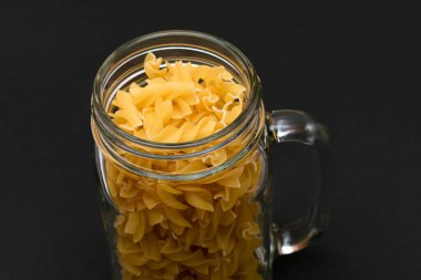 Kara Arkaplanda Cam Kavanoz 'da pişmemiş Fusilli Makarna. Çiğ ve kuru makarna. Sağlıksız ve şişman yiyecekler. İtalyan Kültürü