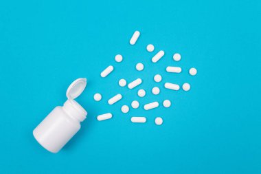 Küresel İlaç Endüstrisi ve İlaç Ürünleri - İlaç Konteynırından Dağılmış Beyaz Haplar veya Tabletler, Mavi Arkaplanda Yatanlar