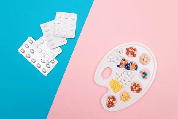 グローバル製薬業界と医薬品 異なる色の錠剤 カプセルをホワイトアートパレット上にピルパッケージがスプリットブルーとピンクの背景に横たわっている フラットレイ — ストック写真