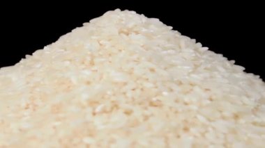 Beyaz Tabakta pişmemiş beyaz pirinç yığını Siyah Arkaplan 'a karşı dönüyor. Çiğ Uzun Taneli Pirinç Yığını. Asya mutfağı ve kültürü. Sağlıklı beslenme malzemeleri. Diyet Yemekler