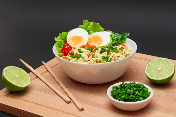 Beautiful Noodle Dish with Green Pea, Carrot, Eggs, Red Hot Pepper and Greens with Chopsticks on Bamboo Cutting Board. Instant Noodles with Vegetables