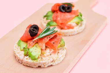 Taze somonlu Rice Cake Sandviçleri, Tahta Kesme Kurulunda Avokado ve Zeytinler. Kolay Kahvaltı 'da. Diyet yemek. Hızlı ve sağlıklı sandviçler. Lezzetli dolgulu kızarmış ekmek. Sağlıklı Beslenme Atıştırması