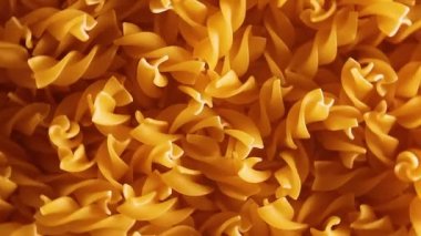 Pişmemiş Fusilli Makarna - Üst Görünüm, Yakın Çekim, Alçak Anahtar Işığı. Şişman ve Sağlıksız Yemek. Kuru Spiral makarna, döner arka plan. İtalyan Kültür ve Mutfağı. Çiğ Altın Makarna deseni. Sağ Çevirme