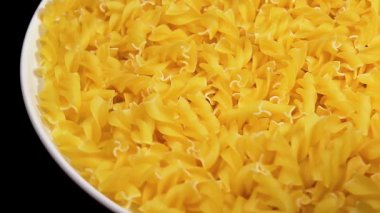 Beyaz Tabakta pişmemiş Fusilli Makarna Siyah Arkaplan 'a karşı dönüyor. Şişman ve Sağlıksız Yemek. Kuru Spiral makarna. İtalyan Kültür ve Mutfağı. Çiğ Altın Makarna