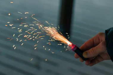 Firecracker 'ı kıvılcımla yakmak. Elinde Petard tutan bir adam. Gürültülü ve tehlikeli yeni yıl eğlencesi. Havai fişeklerle holiganlık. Halka açık yerlerde havai fişek sesleri