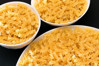 Pişmemiş Fusilli Makarna Siyah Arkaplanda Beyaz Tabakta Yatıyor. Çiğ ve kuru makarna. Sağlıksız ve şişman yiyecekler