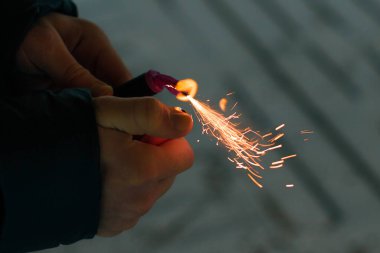 Firecracker 'ı kıvılcımla yakmak. Elinde Petard tutan bir adam. Gürültülü ve tehlikeli yeni yıl eğlencesi. Havai fişeklerle holiganlık. Halka açık yerlerde havai fişek sesleri