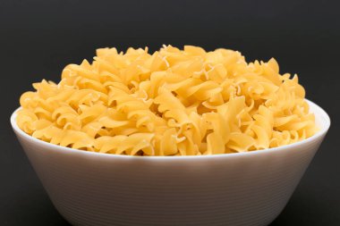 White Bowl 'daki pişmemiş Fusilli Makarna Siyah Masa' da. Çiğ ve kuru makarna. Sağlıksız ve şişman yiyecekler. İtalyan Kültürü