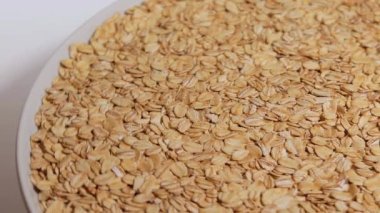 Pişmemiş Yulaf Gevreği Beyaz Plaka 'da Beyaz Arkaplan' a karşı dönüyor. Dağıtılmış Kuru ve Çiğ Yulaf Gevreği. Sağlıklı Kahvaltı ve Beslenme Malzemeleri