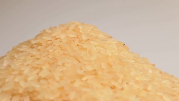 乾燥調理されていないパラボイルドライスヒープ白の背景に対して回転します 生の長粒米の山 アジア料理と文化 健康的な食材 — ストック動画